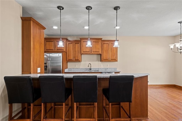 kitchen with light stone countertops, hanging light fixtures, light hardwood / wood-style floors, stainless steel fridge with ice dispenser, and a breakfast bar