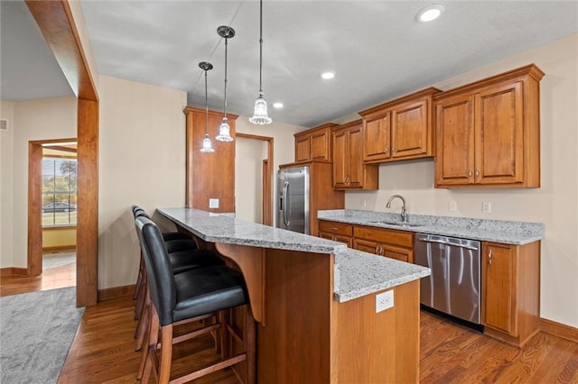 kitchen featuring hanging light fixtures, dark hardwood / wood-style flooring, appliances with stainless steel finishes, a kitchen bar, and light stone counters