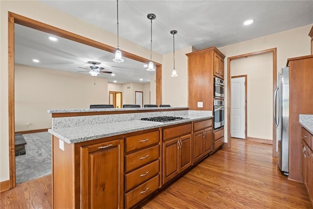 kitchen featuring appliances with stainless steel finishes, light wood-type flooring, a kitchen island, ceiling fan, and pendant lighting