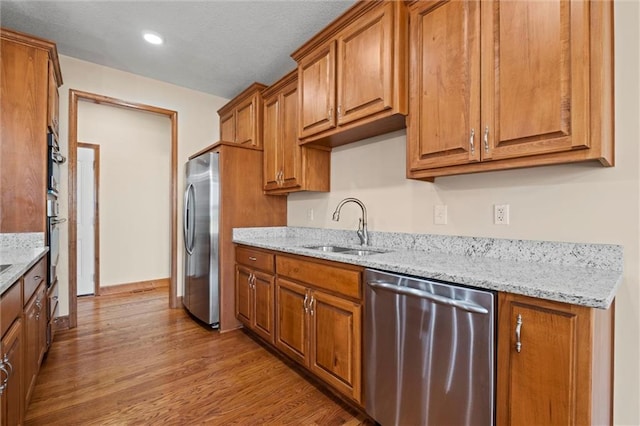 kitchen featuring light stone countertops, light hardwood / wood-style flooring, appliances with stainless steel finishes, and sink