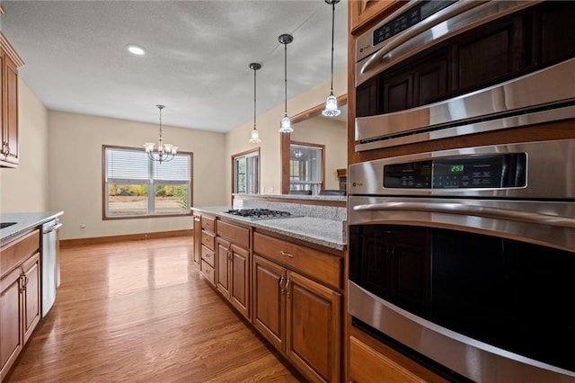 kitchen featuring light stone countertops, light wood-type flooring, stainless steel appliances, a notable chandelier, and decorative light fixtures