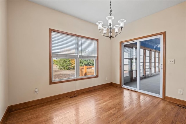 spare room with wood-type flooring and an inviting chandelier