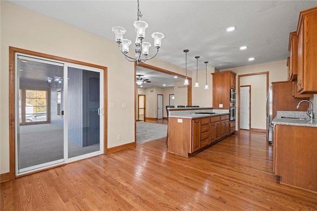 kitchen featuring kitchen peninsula, hanging light fixtures, light wood-type flooring, stainless steel appliances, and sink