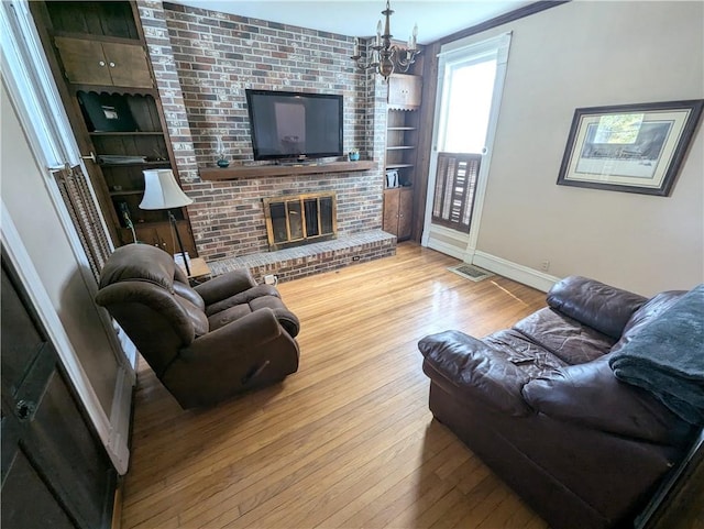 living room with an inviting chandelier, light hardwood / wood-style flooring, built in shelves, and a brick fireplace