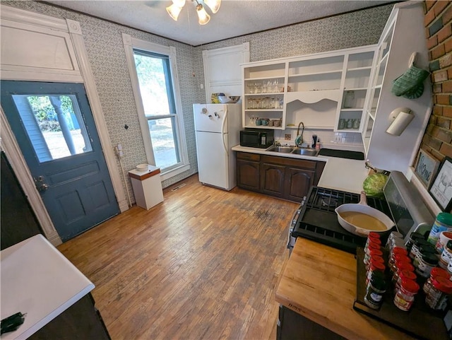 kitchen with sink, a textured ceiling, dark brown cabinets, white fridge, and light hardwood / wood-style flooring