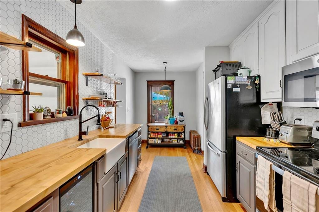 kitchen featuring wood counters, wine cooler, appliances with stainless steel finishes, decorative light fixtures, and light hardwood / wood-style floors