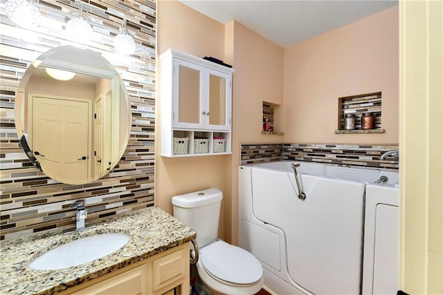 bathroom with a washtub, vanity, toilet, and tasteful backsplash