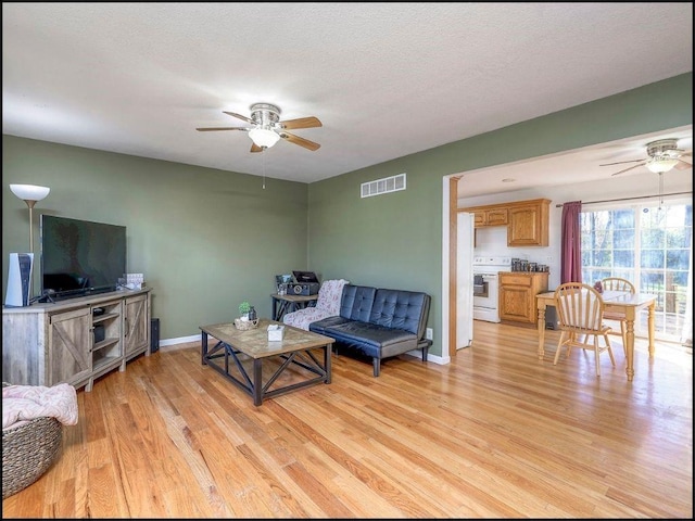 living room featuring a textured ceiling, light wood-type flooring, and ceiling fan