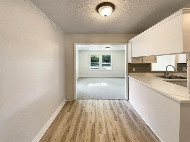 kitchen featuring a textured ceiling, white cabinetry, light hardwood / wood-style floors, crown molding, and sink