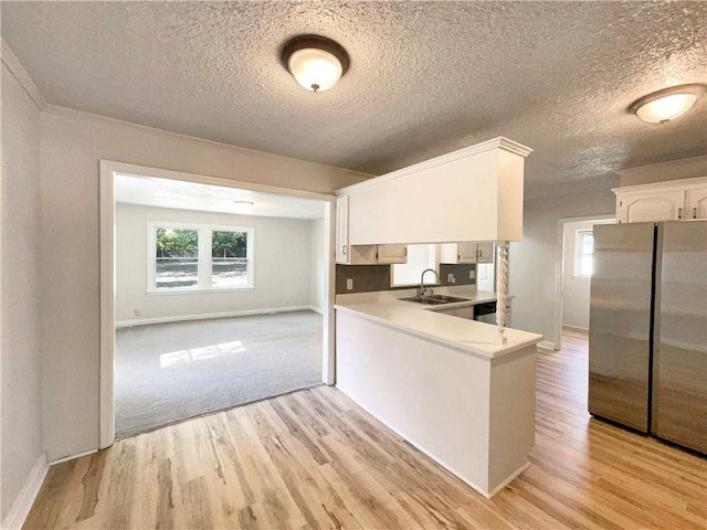 kitchen with white cabinets, a textured ceiling, stainless steel refrigerator, light hardwood / wood-style flooring, and sink