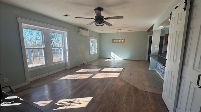 empty room featuring dark wood-type flooring, a wall unit AC, a barn door, and ceiling fan with notable chandelier