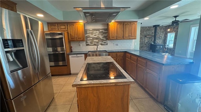 kitchen featuring kitchen peninsula, stainless steel appliances, a wood stove, sink, and light tile patterned floors