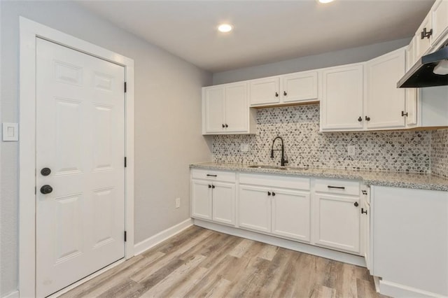 kitchen featuring light stone counters, white cabinetry, backsplash, sink, and light hardwood / wood-style floors