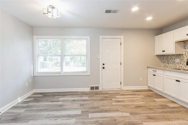 kitchen with tasteful backsplash, white cabinetry, light stone countertops, sink, and light hardwood / wood-style flooring