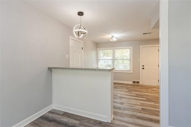 kitchen with kitchen peninsula, hanging light fixtures, hardwood / wood-style flooring, and light stone countertops