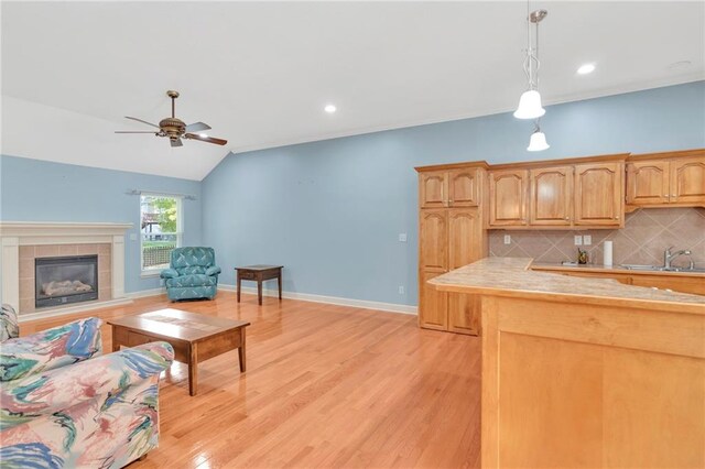 kitchen featuring decorative backsplash, hanging light fixtures, light hardwood / wood-style flooring, a fireplace, and sink