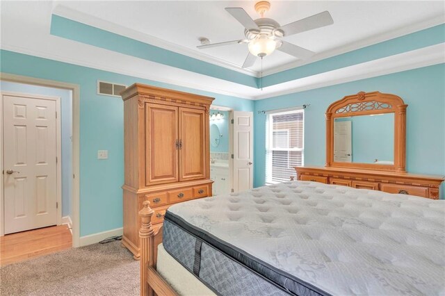 bedroom featuring light carpet, ceiling fan, a tray ceiling, connected bathroom, and crown molding