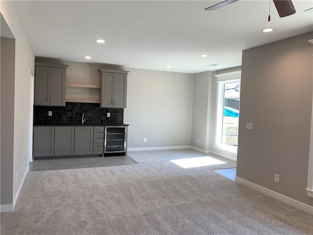 kitchen featuring gray cabinets, backsplash, dark countertops, wine cooler, and light colored carpet