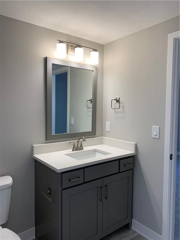 bathroom with a textured ceiling, toilet, vanity, and baseboards