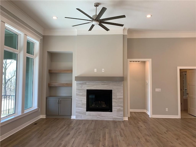 unfurnished living room with a tiled fireplace, built in shelves, baseboards, and ornamental molding