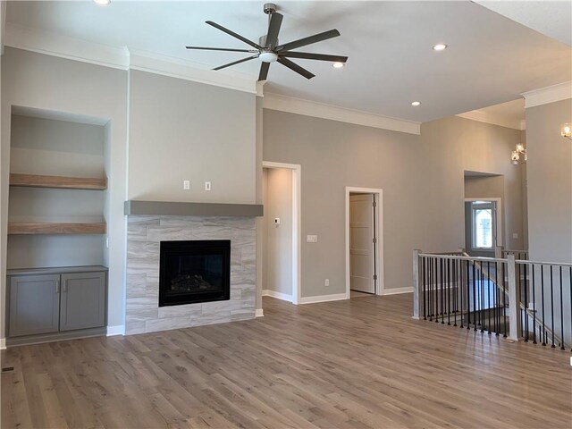 unfurnished living room with a ceiling fan, wood finished floors, crown molding, baseboards, and a tile fireplace