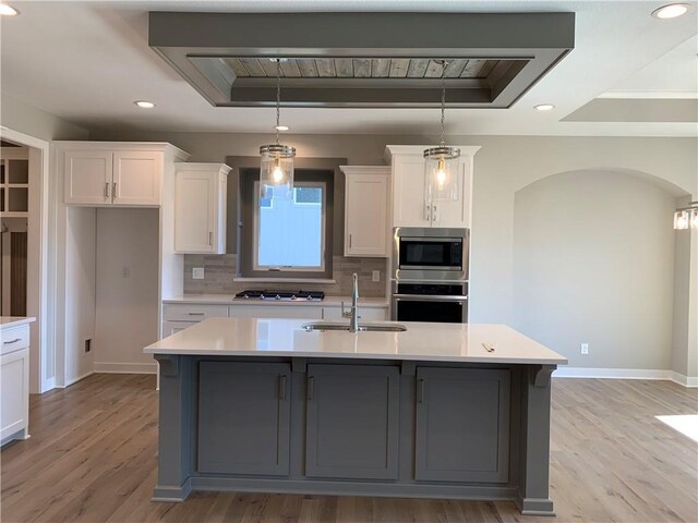 kitchen with a raised ceiling, wall chimney range hood, arched walkways, and stainless steel appliances