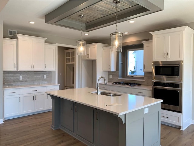 kitchen with visible vents, dark wood-type flooring, a tray ceiling, appliances with stainless steel finishes, and a sink