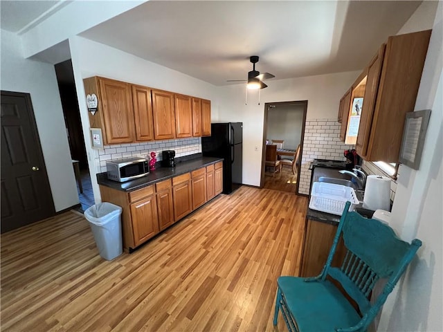 kitchen featuring black fridge, backsplash, sink, light hardwood / wood-style floors, and ceiling fan