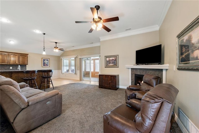 living room with ceiling fan, crown molding, bar, light carpet, and a tiled fireplace