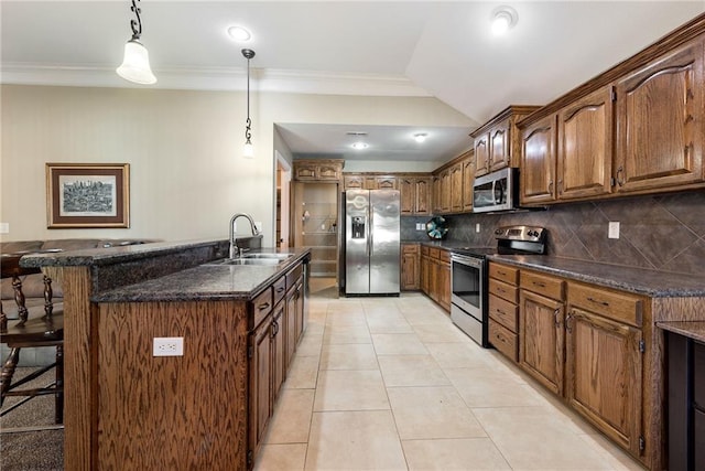 kitchen with appliances with stainless steel finishes, tasteful backsplash, sink, hanging light fixtures, and an island with sink