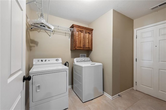 laundry room featuring cabinets, independent washer and dryer, a textured ceiling, and light tile patterned floors