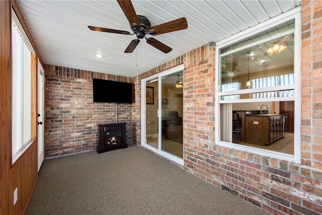 unfurnished sunroom with ceiling fan, a wood stove, sink, and a wealth of natural light