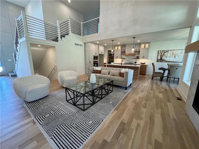 living room featuring sink, light hardwood / wood-style flooring, and a towering ceiling