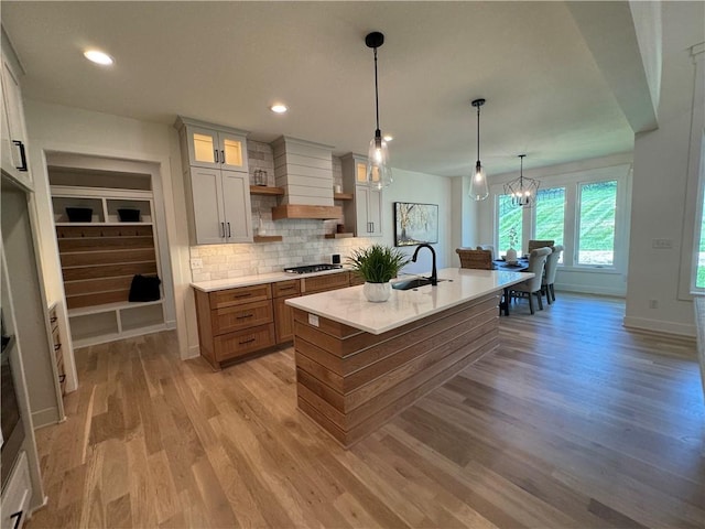 kitchen featuring a kitchen island with sink, light hardwood / wood-style flooring, sink, a notable chandelier, and white cabinetry