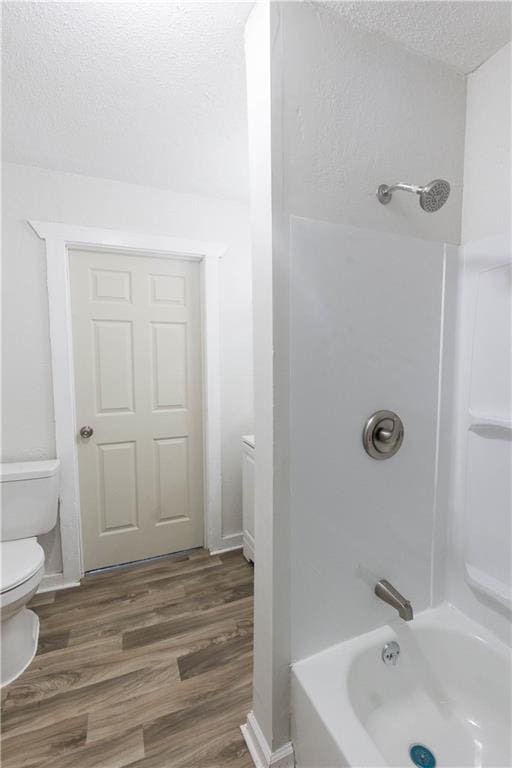 bathroom with toilet, shower / bathing tub combination, hardwood / wood-style floors, and a textured ceiling