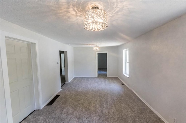 empty room with a notable chandelier, carpet floors, and a textured ceiling