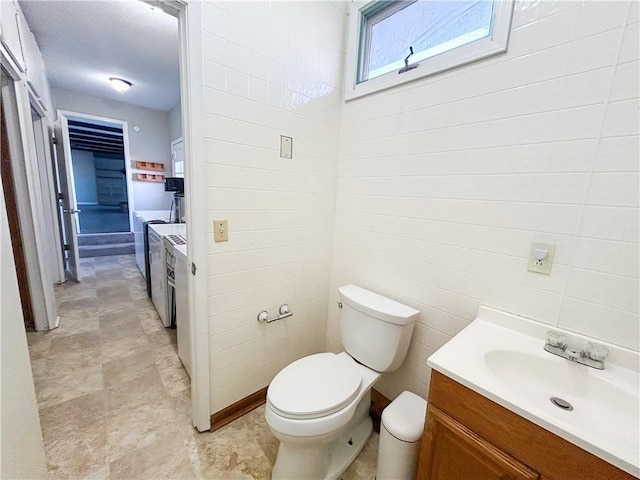 bathroom with independent washer and dryer, vanity, toilet, and tile walls