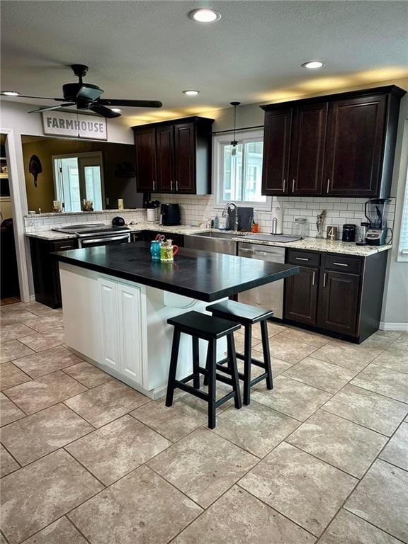 kitchen with ceiling fan, a breakfast bar area, sink, pendant lighting, and stainless steel appliances