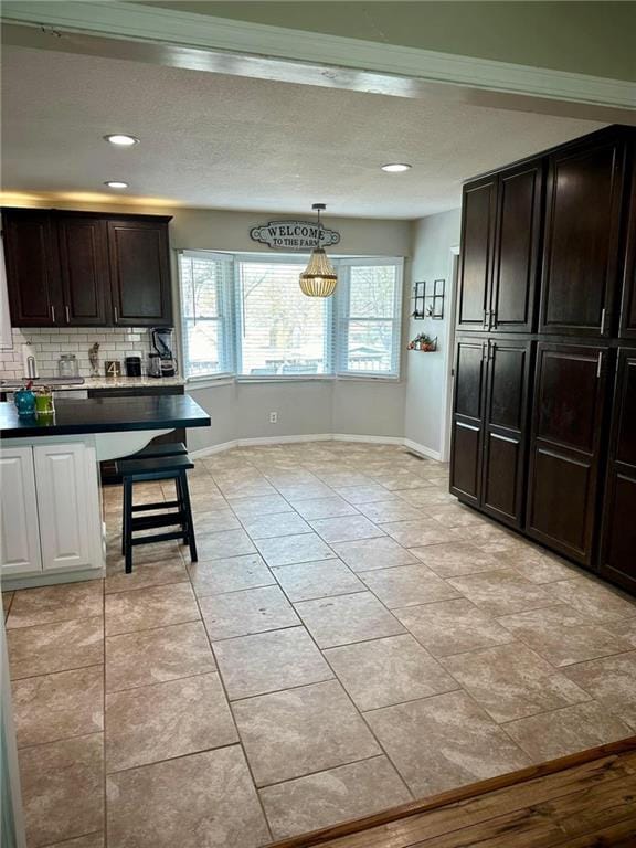 kitchen featuring dark brown cabinets, light tile patterned floors, hanging light fixtures, and backsplash