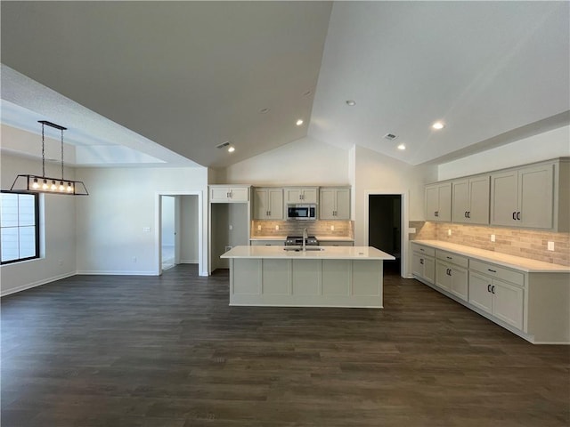 kitchen with decorative light fixtures, an island with sink, sink, backsplash, and dark wood-type flooring