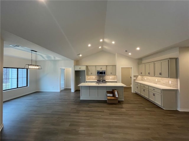 kitchen featuring sink, dark hardwood / wood-style flooring, decorative backsplash, hanging light fixtures, and a center island with sink