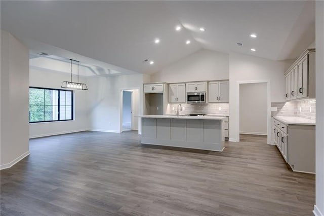 kitchen with light countertops, stainless steel microwave, decorative backsplash, and wood finished floors