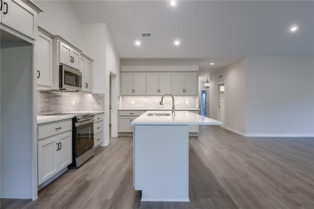 kitchen featuring a sink, stainless steel appliances, backsplash, visible vents, and a center island with sink