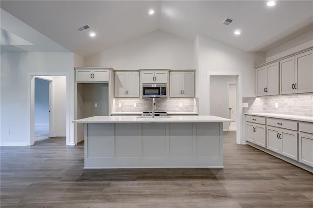 kitchen featuring stainless steel microwave, visible vents, a center island with sink, and tasteful backsplash