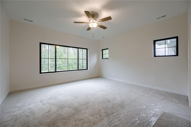 carpeted spare room featuring baseboards, ceiling fan, and visible vents