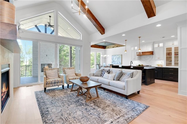 living room featuring beam ceiling, a healthy amount of sunlight, a large fireplace, and light wood-type flooring