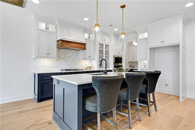 kitchen with white cabinetry, decorative light fixtures, light hardwood / wood-style floors, and an island with sink