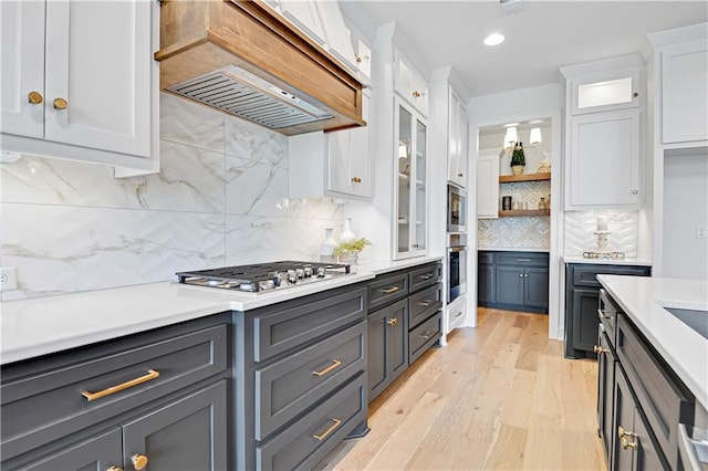 kitchen with white cabinetry, tasteful backsplash, light hardwood / wood-style flooring, and custom exhaust hood