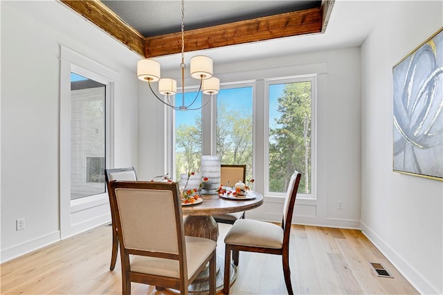 dining space featuring light hardwood / wood-style floors, a notable chandelier, a tray ceiling, and a healthy amount of sunlight