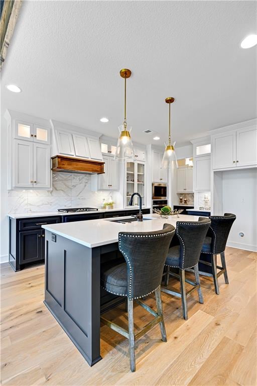 kitchen with a large island with sink, a breakfast bar, white cabinetry, pendant lighting, and sink